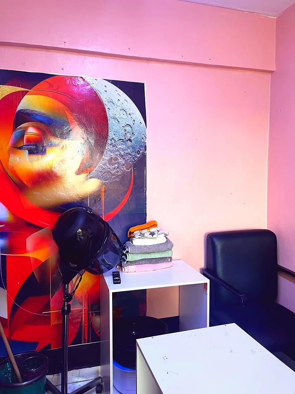Vibrant mural of a woman's face beside a hood dryer and freshly folded towels