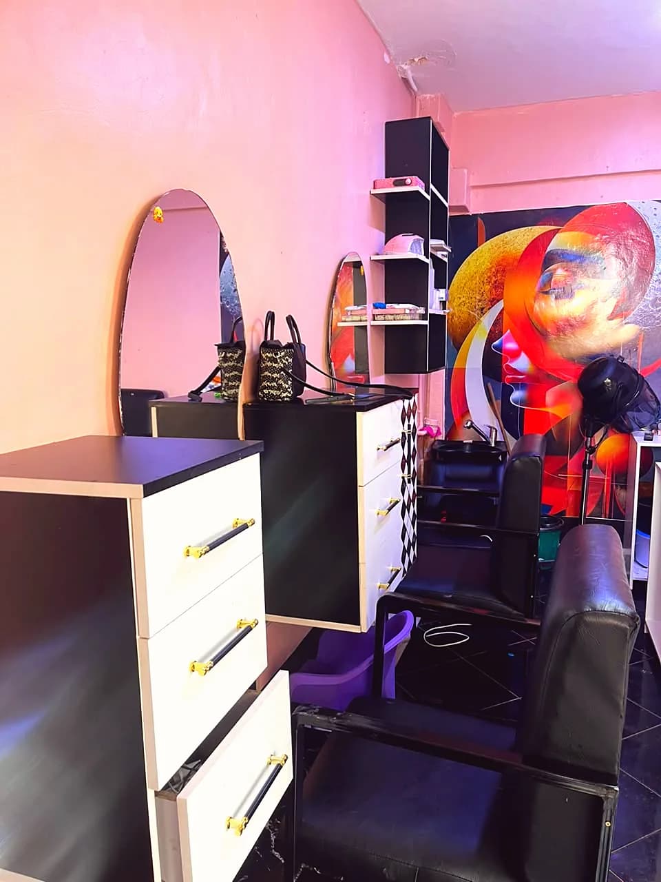 Styling stations at Heavens Beauty and Spa with oval mirrors, white drawers with gold handles and a colourful wall mural